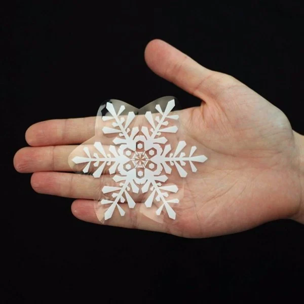 A hand holding a white double-sided electrostatic snowflake sticker against a black background.