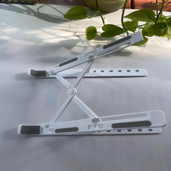 White folding laptop stand collapsed flat on a desk beside a green houseplant