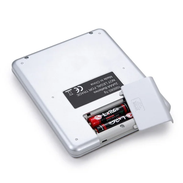 Back of a silver digital pocket scale with open battery compartment holding AA batteries and a specification label