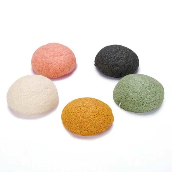 Five round konjac facial sponges in white, pink, gray, green and orange arranged on a plain white background