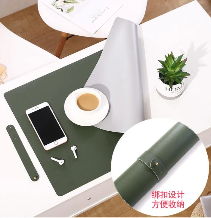 Green PU leather desk pad on a white desk with a smartphone, coffee, and earphones, featuring a rolled-up view showing a strap closure.