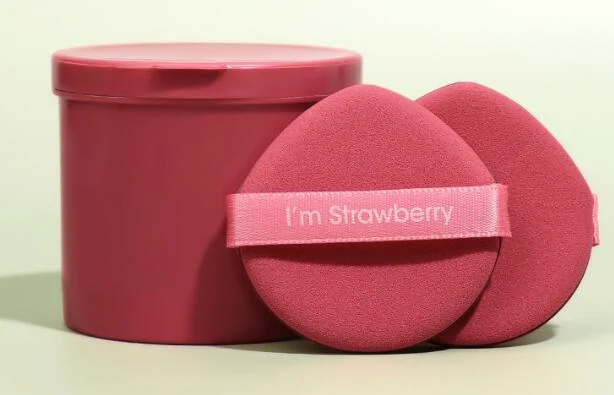 Pink fan-shaped non-latex powder puffs with printed ribbon band beside a round pink plastic storage canister