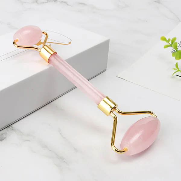 Pink rose quartz facial roller with gold metal frame resting on a