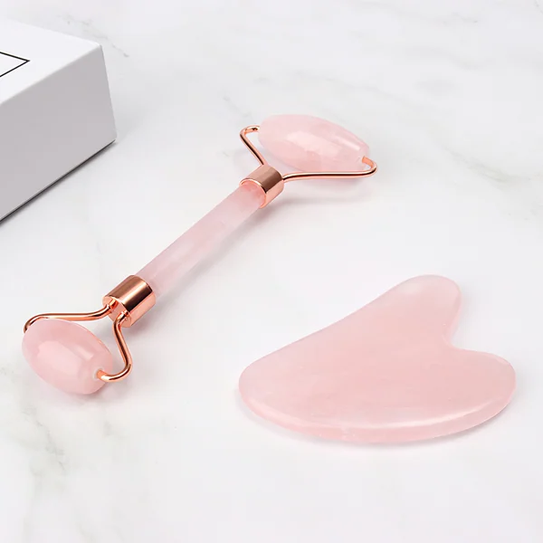 Pink rose quartz facial roller with copper frame and heart-shaped gua sha stone on white marble with white box