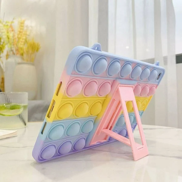 Pastel rainbow pop-it silicone iPad case shown from the back with kickstand open, standing on a marble table