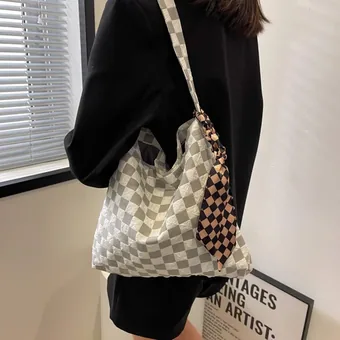 Person modeling a large checkerboard canvas shoulder bag with a scarf tied to the handle.