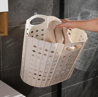 Foldable wall-mounted laundry basket holding towels on a tiled bathroom wall