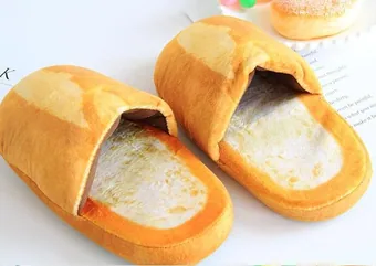 A pair of plush home slippers designed to look like slices of golden-brown bread with a white interior.