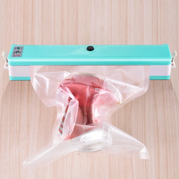 Teal and white vacuum food sealer on a wooden surface with a plastic bag containing raw meat.
