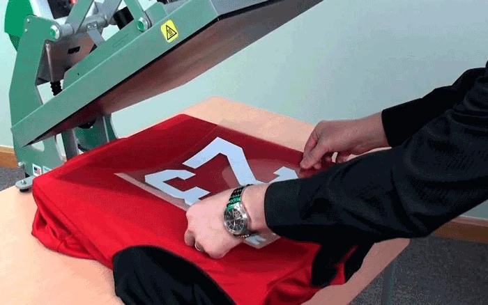 Operator pressing a heat transfer onto a red T-shirt with a heat press