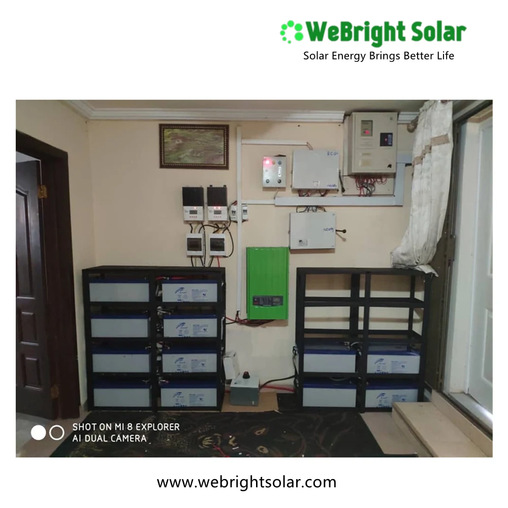 Wall-mounted solar inverter and charge controllers above two racks of batteries in an indoor room.