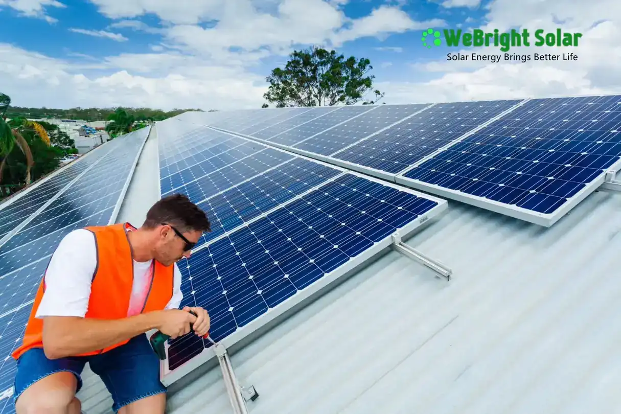 Technician in an orange safety vest installing solar panels on a corrugated metal roof.