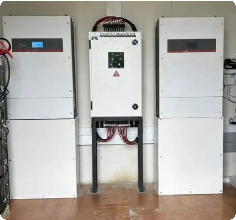 Solar PV combiner box mounted on a stand between two white electrical cabinets.