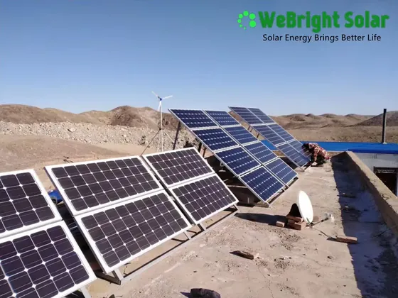 Multiple solar panels installed on a concrete rooftop with a small wind turbine in the background.