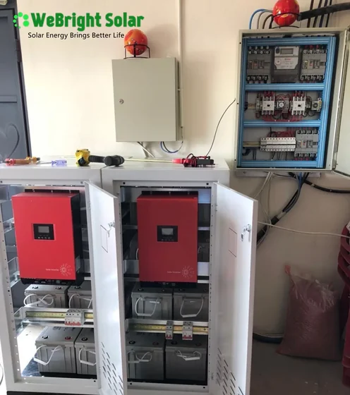 Open electrical cabinets containing red solar inverters and battery banks mounted on a wall.