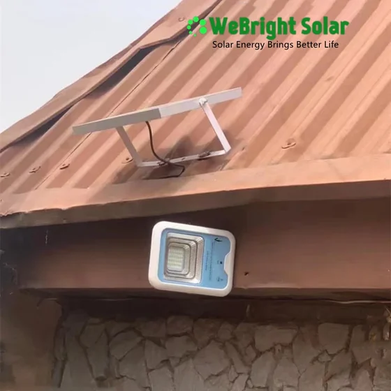 Solar flood light fixture mounted on a roof beam with panel on corrugated metal roof