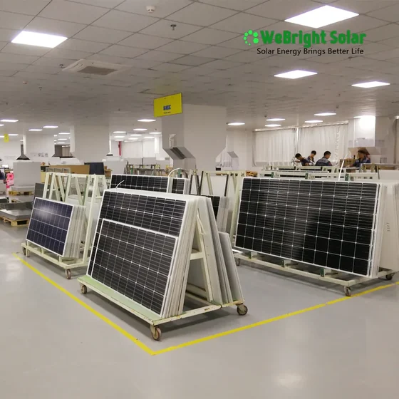 Solar panels resting on wheeled racks inside a brightly lit manufacturing facility.