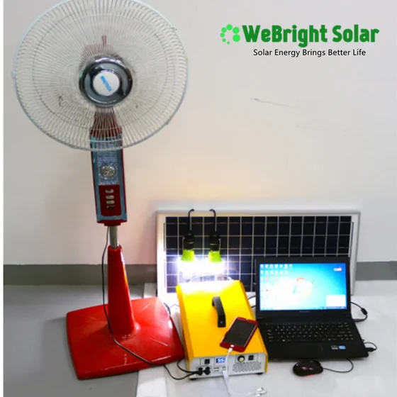 A red pedestal fan, solar panel, yellow power unit, laptop, and lights arranged on a floor.