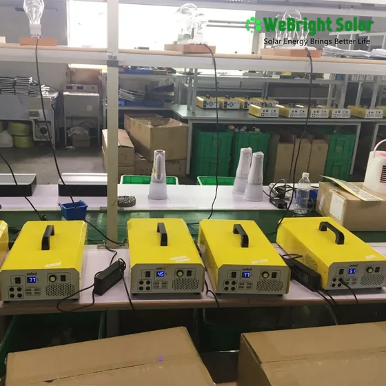 A row of yellow electronic devices with digital displays lined up on a testing table in a factory, with lightbulbs above them.