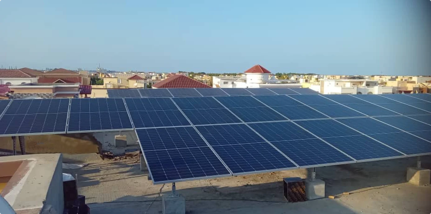 Solar panels installed on a flat rooftop overlooking a residential area under a clear sky.