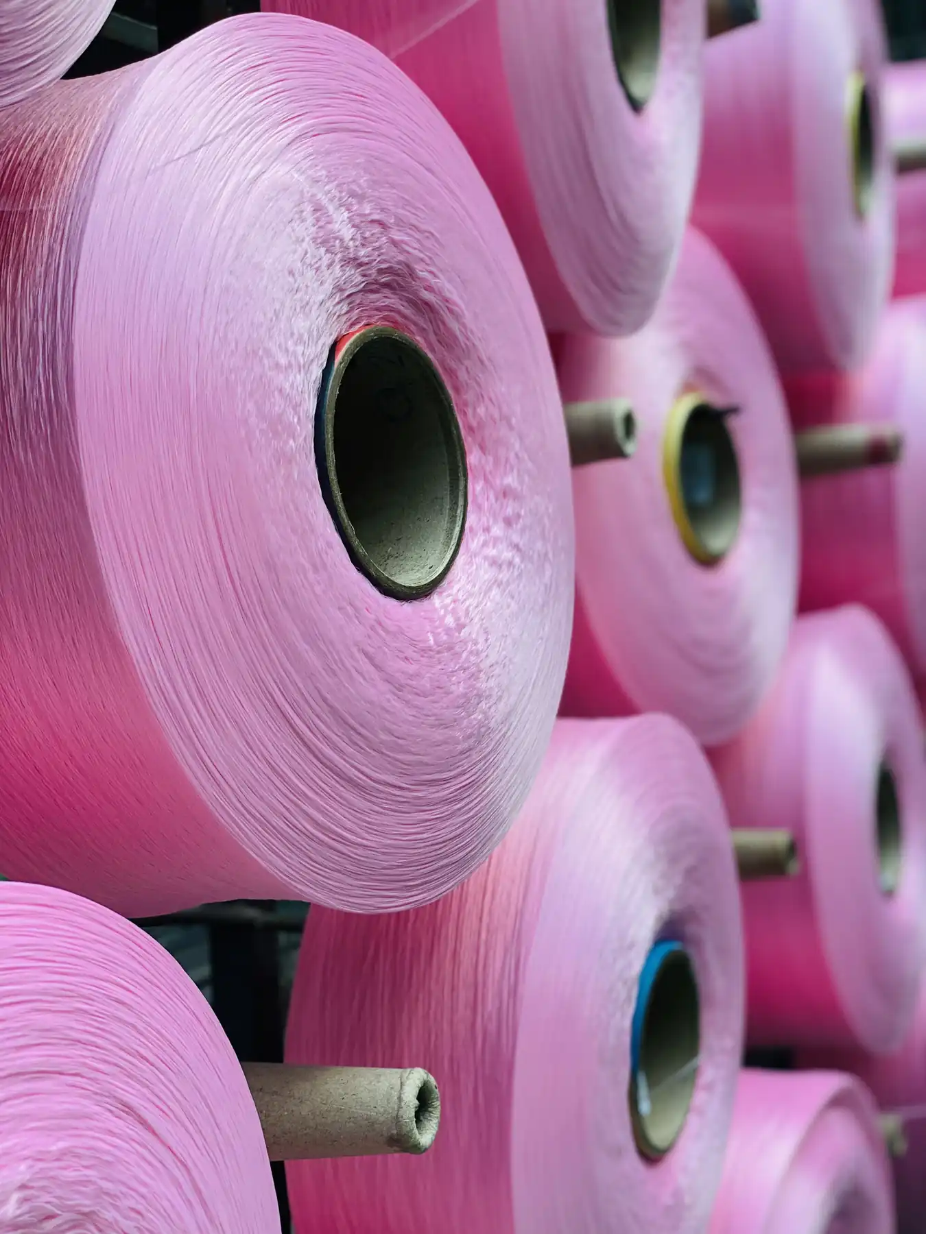 Cones of pink polyester yarn loaded on the creel before warping