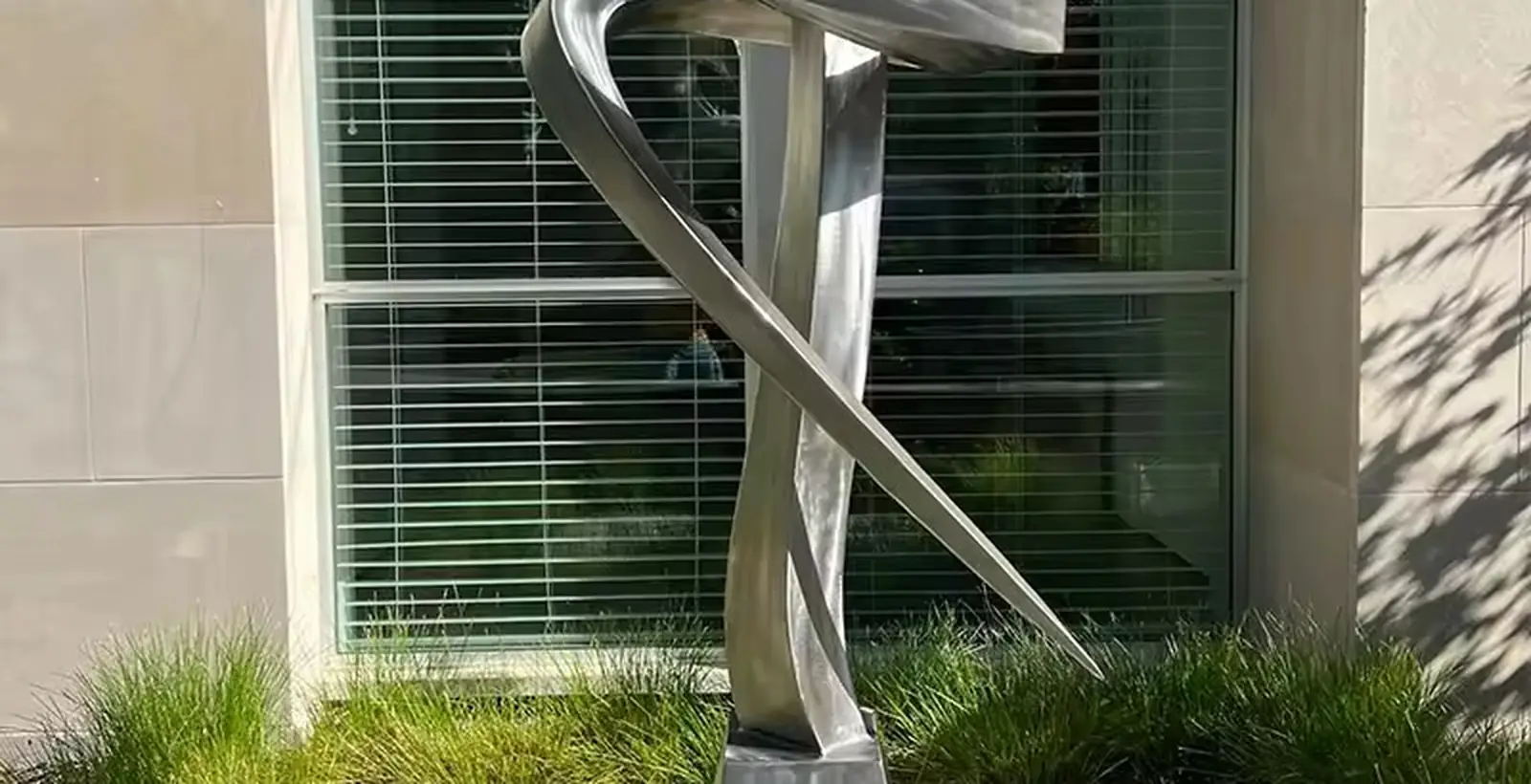 Mirror polished stainless steel abstract sculpture installed in a planted bed outside an office building