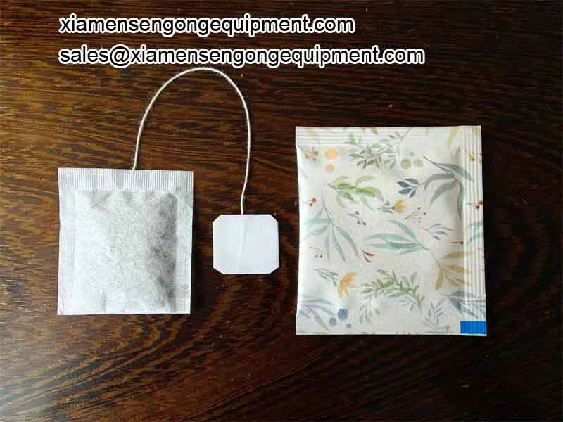 A filter paper inner tea bag with thread and tag beside its printed outer envelope