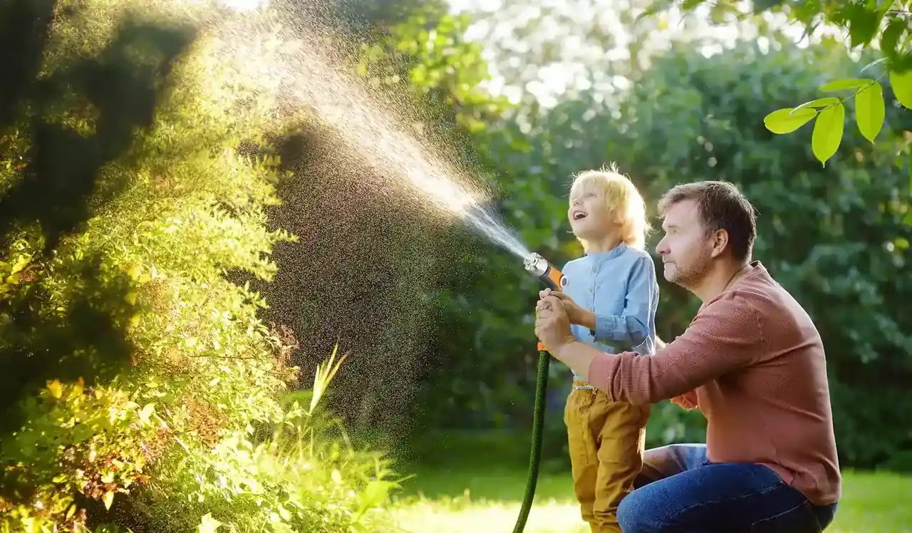 Adult and child watering a garden lawn together