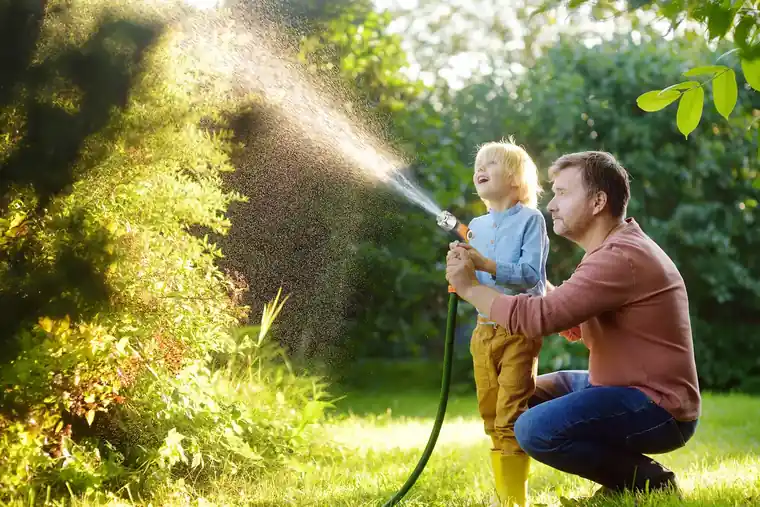 Adult and child watering a garden together with a spray gun