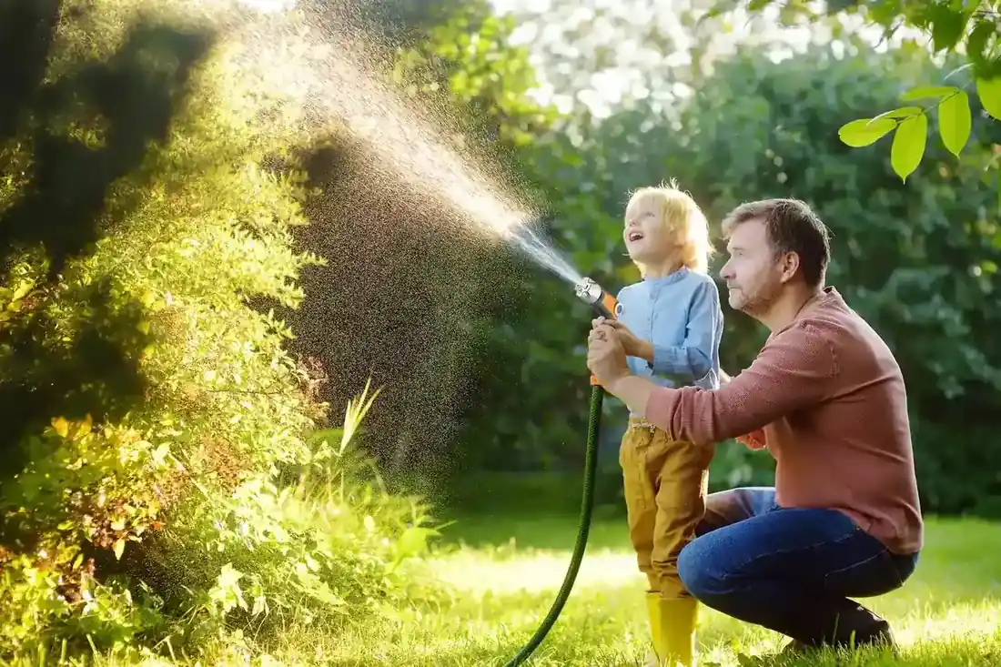 Adult and child watering a garden together with a spray gun