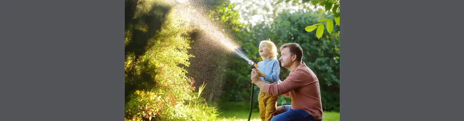 Adult and child using a garden spray gun on a lawn