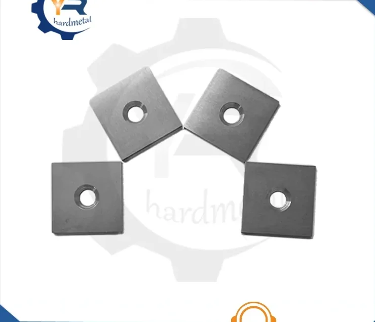 Four square tungsten carbide inserts with center mounting holes arranged on a white background