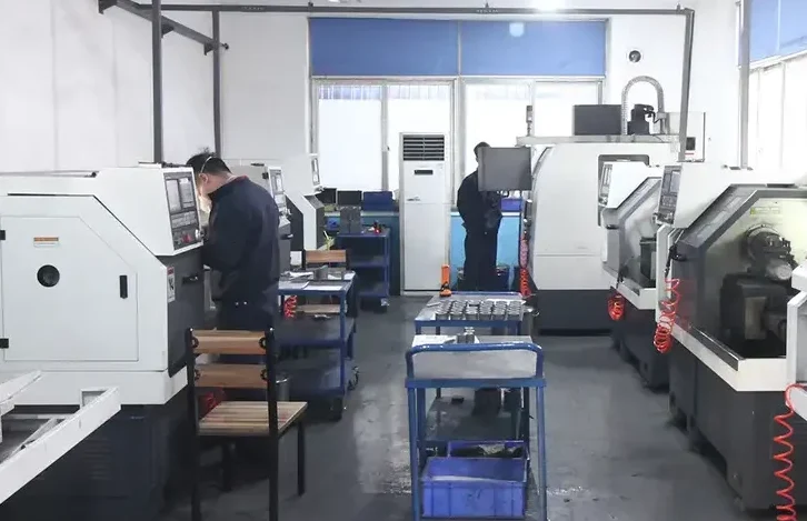 Workers operating CNC lathe machines in an industrial workshop with tool carts and blue storage bins
