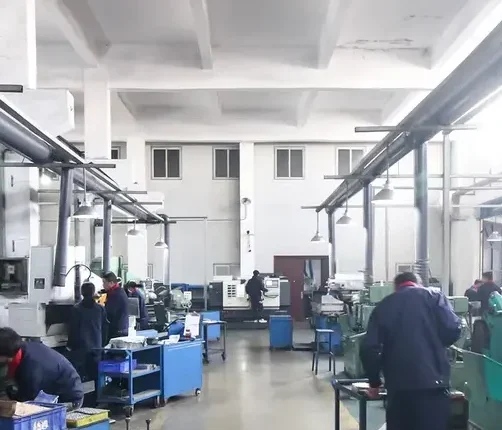 Workers operating machine tools inside a machining workshop with blue tool carts and overhead ducting