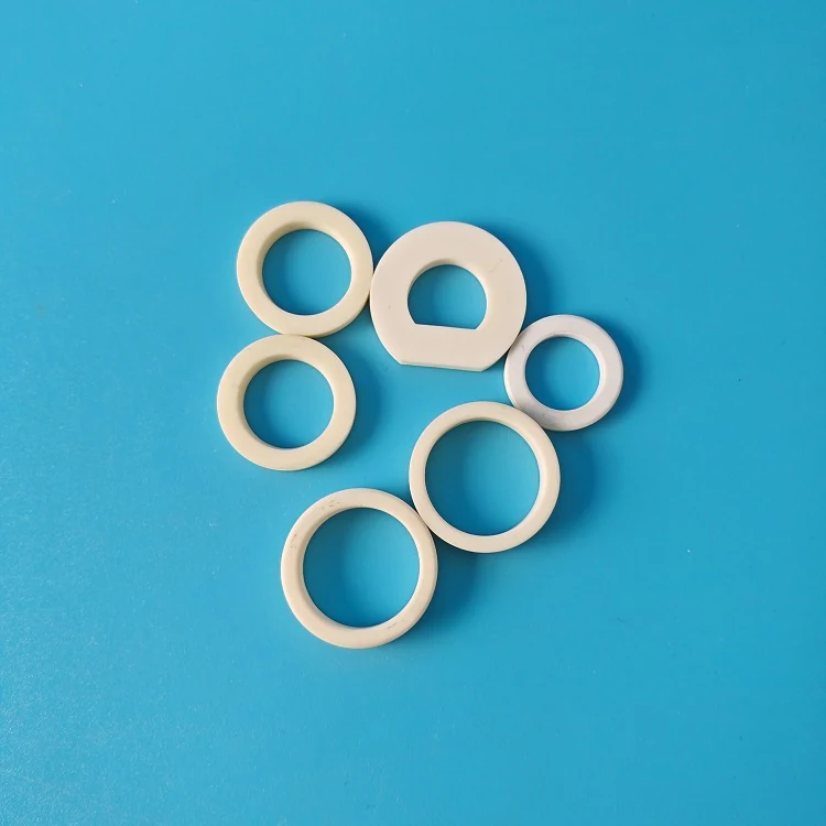 Four white alumina ceramic rings with external serrations on a blue background