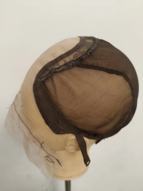 כיפה חומה על ראש מנקן בז' במבט מלמעלה ומעט מאחור, פאנל ארוג עדין על הכתר מוקף ברצועת לייס מעוטרת, עם רצועה וקליפס תלויים בעורף
